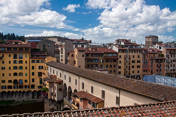 Elevated view of historic residential buildings lining the Arno River in the old city of Florence, Italy, under clear daylight conditions.