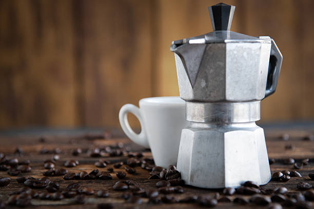 White coffee cup and moka pot placed on coffee beans against wooden background.