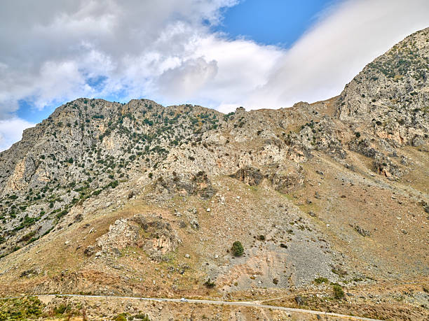 Crete landscape in Greece showcases rugged mountains, rocky hills, and an arid hillside beneath a bright blue sky with white clouds. This natural outdoor scene highlights Greek terrain and scenery, perfect for travel, nature, tourism, and adventure stock projects celebrating Crete and Greece.