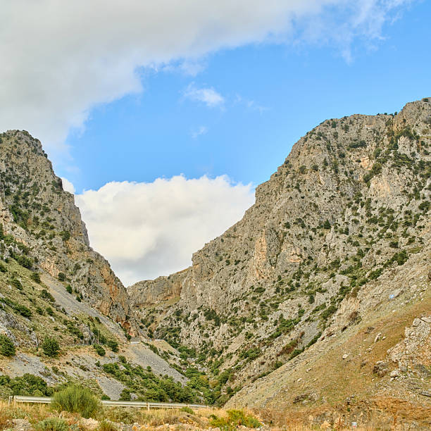 A dramatic Crete gorge in Greece reveals rugged mountain walls and a quiet valley. The scene showcases a blue sky, rocky cliffs, and scattered greenery, creating a powerful landscape perfect for travel, nature, and adventure photography. Ideal for stock listings of outdoor, hiking, and scenic imagery.