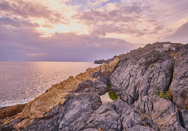 Crete, Greece coastal path along rugged cliffs at sunset. A serene Mediterranean landscape with rocky terrain, low vegetation, and a calm sea to the left. Perfect for travel, nature, hiking, and scenic imagery celebrating coastal beauty and peaceful sunset moments in Greece.