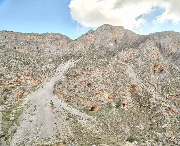 Crete landscape in Greece showcases rugged mountains, rocky hills, and an arid hillside beneath a bright blue sky with white clouds. This natural outdoor scene highlights Greek terrain and scenery, perfect for travel, nature, tourism, and adventure stock projects celebrating Crete and Greece.