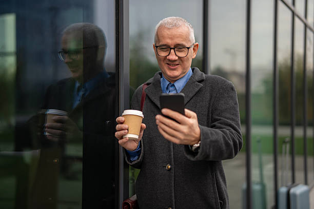 istock Mature adult man smiling, holding coffee and using smartphone 2256153199