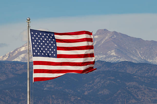 US flag flying with the Rocky Mountains of Colorado in the background.