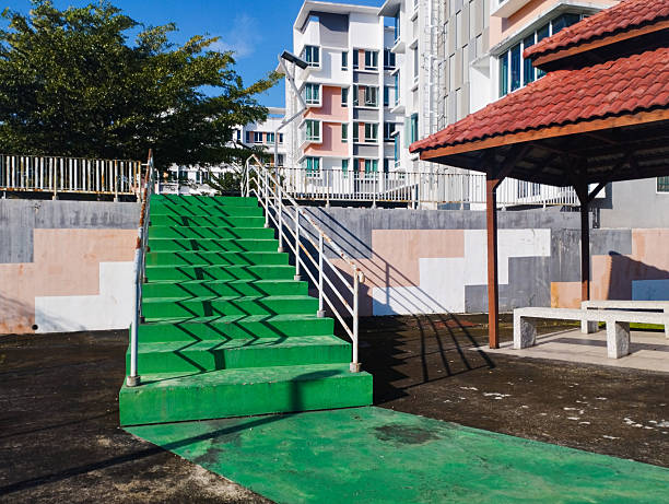 A wide green staircase and wooden gazebo in a residential park, set against modern apartment buildings and a clear blue sky.