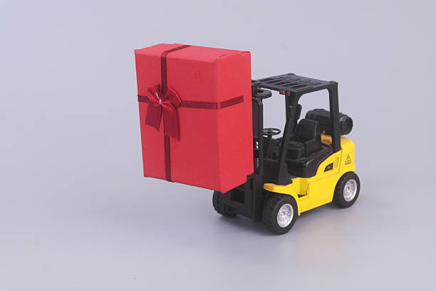 Yellow forklift truck carrying red gift box on grey background
