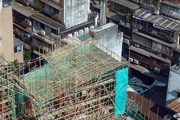 Dense urban area in Hong Kong, where a building is encased in traditional bamboo scaffolding covered with a turquoise-colored safety net