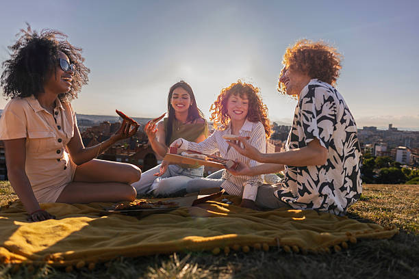 Diverse friends enjoying pizza picnic outdoors at sunset
