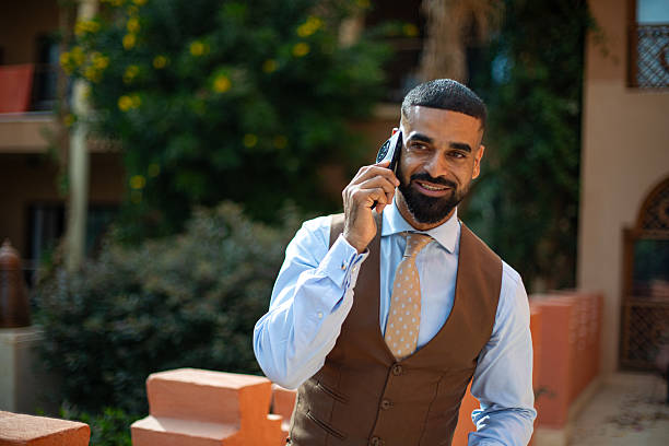 Confident mid adult man conducting business call with smartphone, smiling outdoors