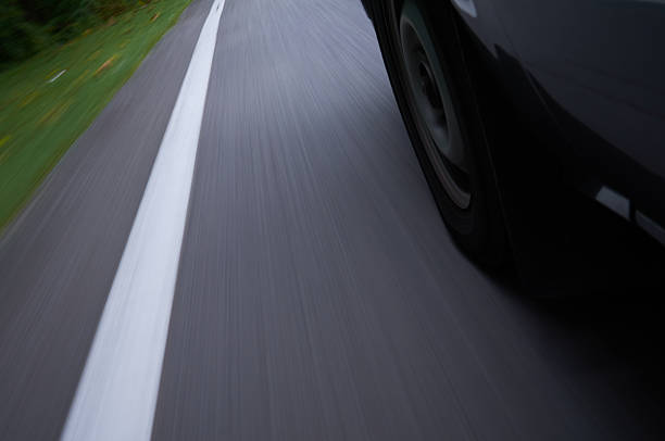 Close up view of moving car wheel on asphalt road with motion blur effect. Transportation, driving, speed, travel and automotive safety concept