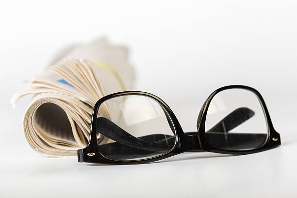 Large vintage reading glasses rest on a book in night light with light reflections on the lenses on a wooden table, macro shot.