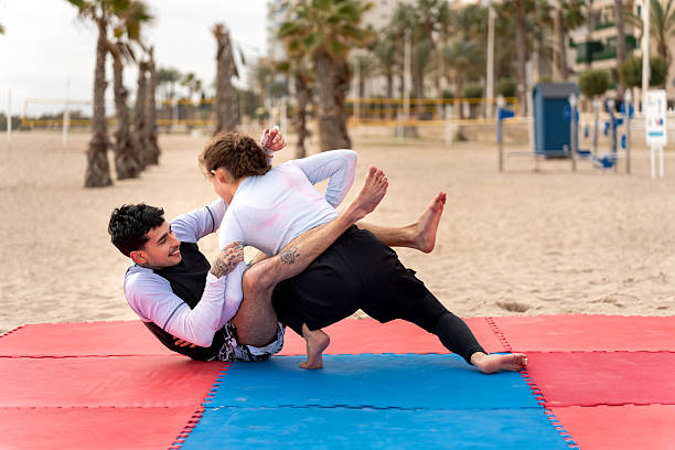 Two athletes in white martial arts uniforms practicing close-contact wrestling technique on blue-green mat. Practitioners demonstrate advanced body control and submission positioning during intense training session.