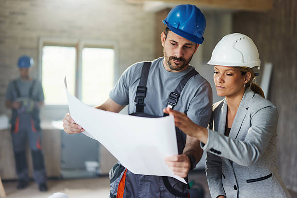 istock Female inspector and manual worker reading plans at renovating home. 2256201856