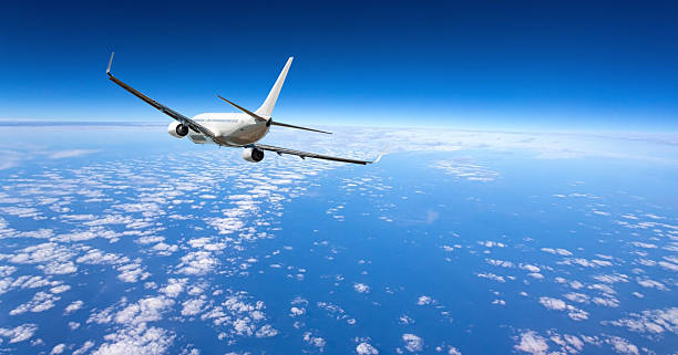 White airplane flying over a vast layer of white clouds under a clear blue sky