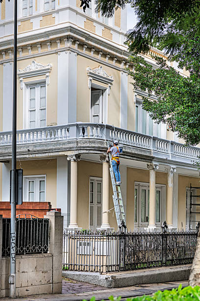 Santa Cruz, Tenerife, Spain, Europe - December 20th 2025: A man is seen standing on a ladder while painting the exterior of a traditional Spanish villa in Santa Cruz, the main city of Tenerife in the Canary Islands. The photo shows routine maintenance work on a classic architectural style commonly found in the region.