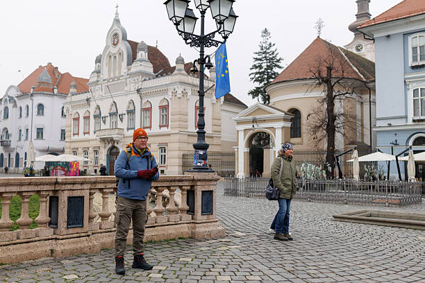 Full length shot of mature man taking photos on his smart phone while visiting old European town with his friends during winter vacation