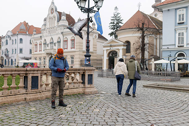 Full length shot of mature man taking photos on his smart phone while visiting old European town with his friends during winter vacation