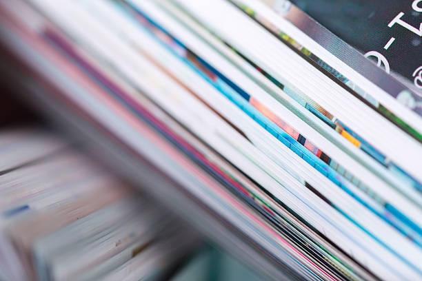 Stacked magazines are arranged on a table, revealing colorful covers and pages.