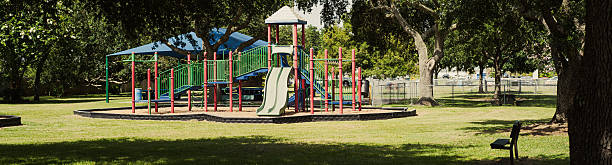 A close-up of two bright red swings hanging from a blue metal frame in a playground. The colorful swings contrast with the green grass below, creating a playful and inviting scene.