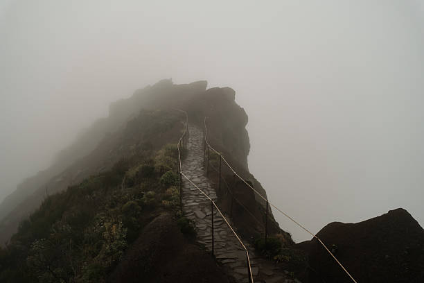Empty foggy mountain ridge path with stone steps and rope railing disappearing into dense mist volcanic rock formations. Madeira, Portugal
