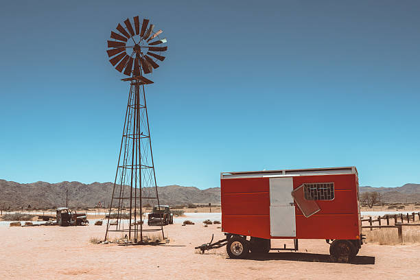 red trailer in front of abandoned vintage car wrecks resting in the sand of Namib dessert