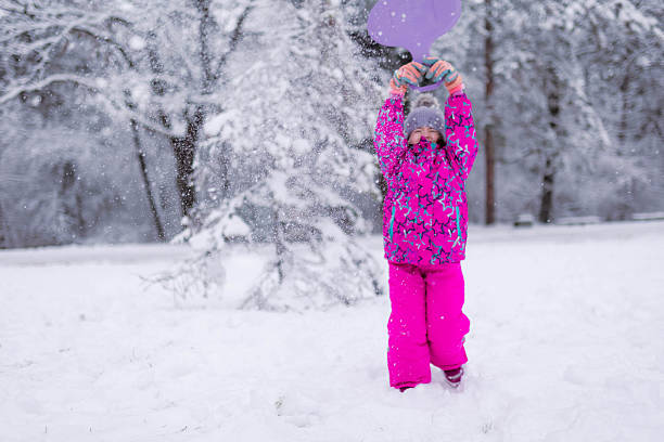 Child dressed in winter clothing plays with snow and smiles while throwing it into the air. Concept of winter season, joy, and outdoor recreation.