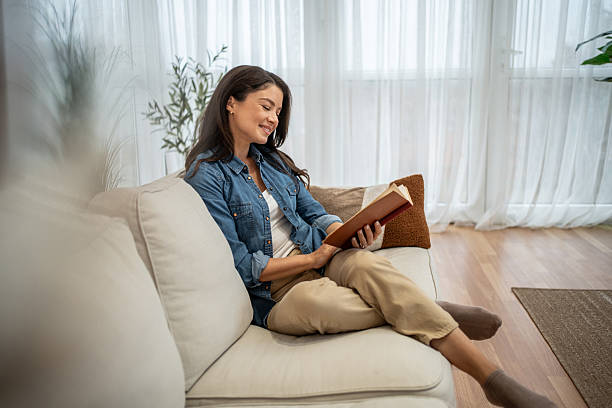 istock Relaxed young woman reading book on comfortable sofa at home 2256227265