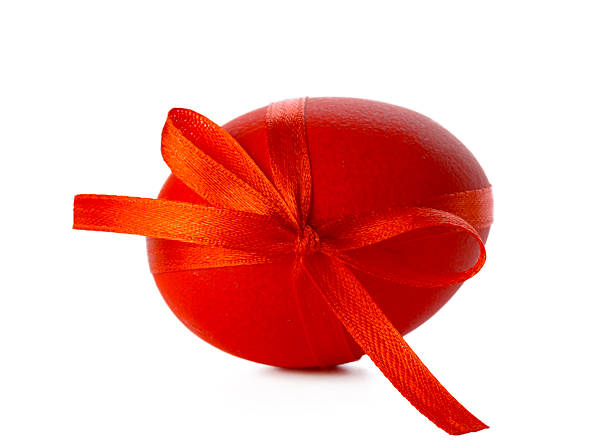 A red egg sits on a white background, wrapped with a shiny ribbon for a spring event.