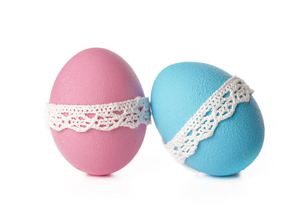 Two brightly colored eggs, one pink and one blue, sit side by side with lace bands around them.