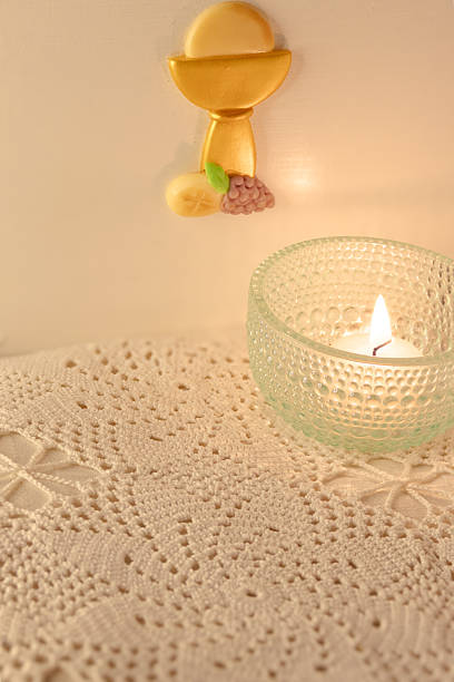Religious scene with a candle on a white crocheted tablecloth and a Eucharistic image in the background. Concept of faith and religiosity.