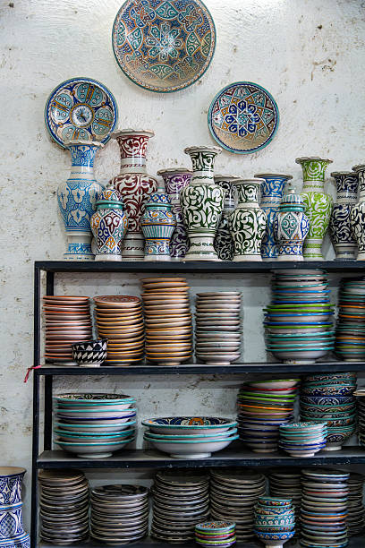 Vibrant ceramic vases and plates from a Moroccan workshop in Fes line a shelf, showcasing intricate patterns and colorful glazes. Rich textures evoke craft, tradition, and travel-inspired home decor.