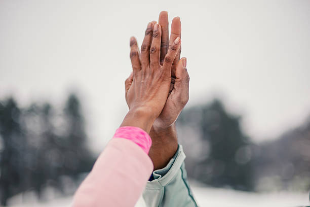 Two diverse adults high-fiving outdoors in winter, celebrating teamwork, partnership and shared goals with joyful connection, unity and supportive collaboration