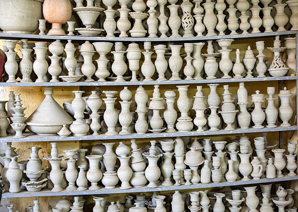 Densely packed display of white pottery on metal shelves in Fes, Morocco. Classic vase shapes, handmade craft, and warm light evoke traditional Moroccan artisan markets.