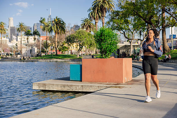 A young adult woman jogging alone in an urban park during daytime. The series highlights fitness, endurance, and active living, showing natural motion and focus during an outdoor workout in a public green space.