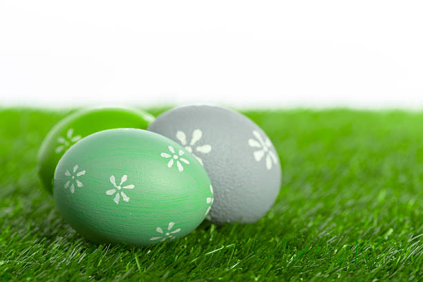 Painted eggs in shades of green and gray sit on grass during spring festivities.