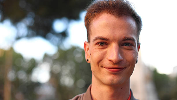 Young handsome man with blue eyes smiling cheerfully at the camera, showing happiness and positive emotions in outdoor setting