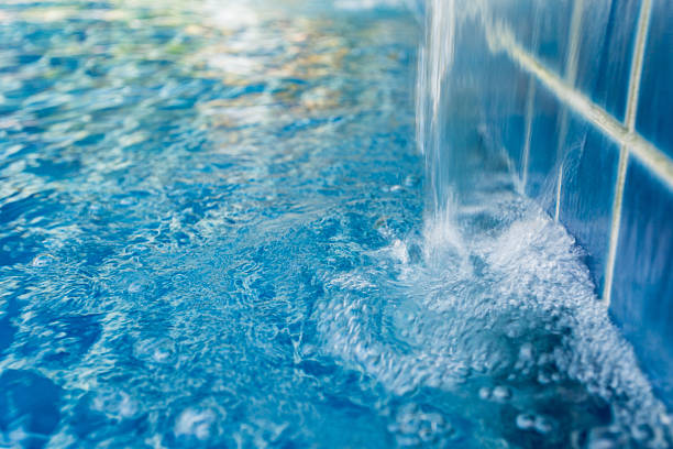 Water streams down from a tiled wall into a clear pool, creating ripples on the surface.