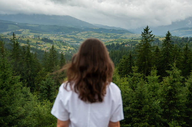 Back view of a young woman looking at beautiful mountain valley under cloudy sky