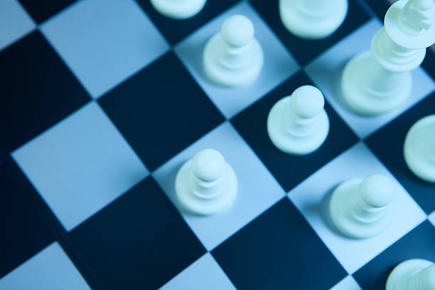 White chess pieces on the chessboard in blue tone. Selective focus.