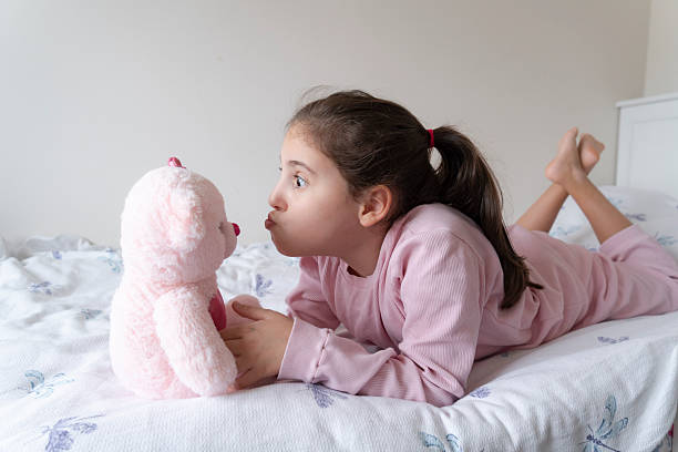 Little girl, playing with teddy toy in a bed