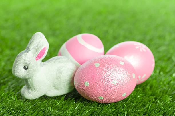 A small rabbit sits next to pink eggs on green grass during a spring celebration.