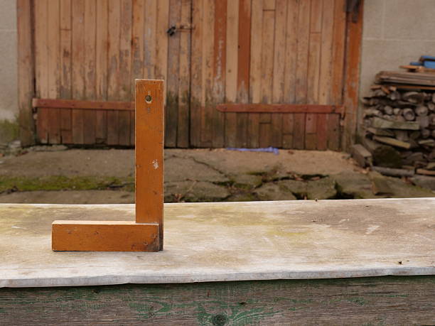 Wooden carpenter square standing on a table against old utility doors in a rural yard.