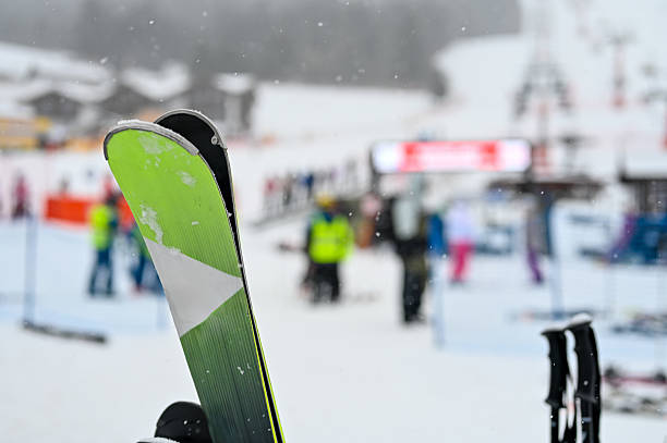 Skier holding ski equipment at a snowy ski resort with people in the background