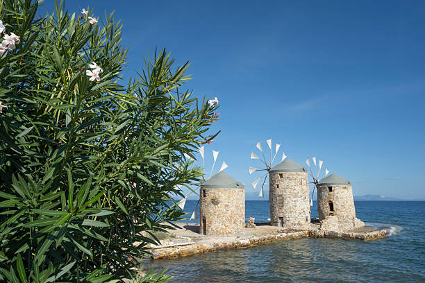 Old traditional windmills at beach of Chios Town on Chios Island in Greece on a on sunny day in late summer (or early autumn), with sea waves and light puffy clouds. Windmills have been used on Greek islands for grinding cereal grains for hundreds of years. These mills were originally built more than 100 years old and has been restored in recent years. For the mills to function, sails are mounted between the wooden spikes.