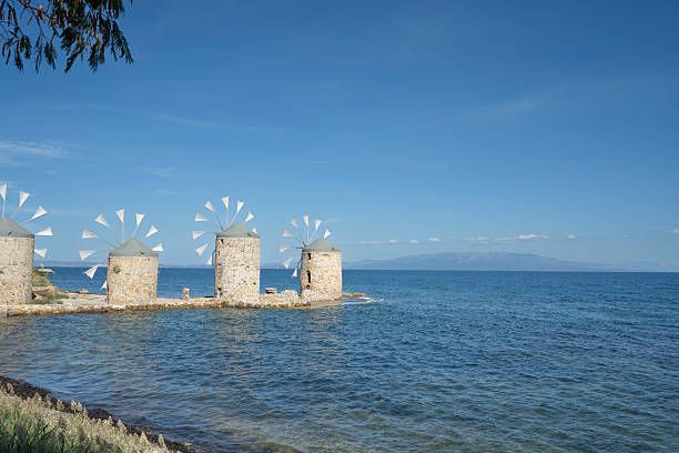 Old traditional windmills at beach of Chios Town on Chios Island in Greece on a on sunny day in late summer (or early autumn), with sea waves and light puffy clouds. Windmills have been used on Greek islands for grinding cereal grains for hundreds of years. These mills were originally built more than 100 years old and has been restored in recent years. For the mills to function, sails are mounted between the wooden spikes.