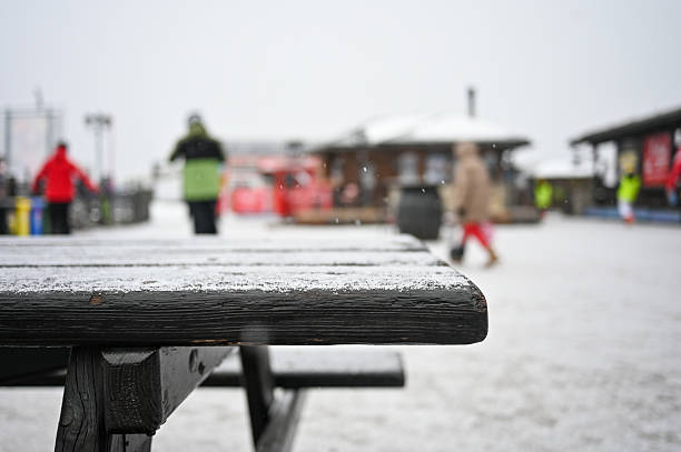 Wooden table covered in snow with blurred people walking through a winter ski resort