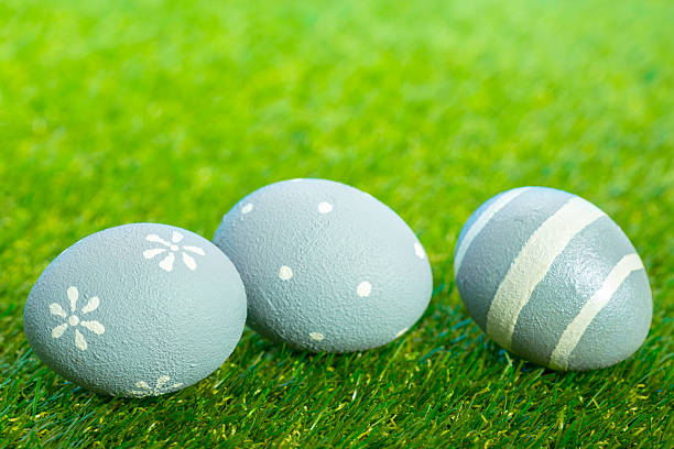 Three painted eggs are resting on fresh green grass during a spring event or craft activity.