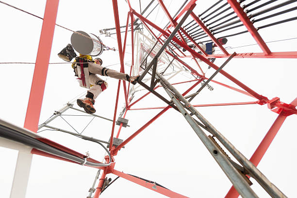 High angle specialized work on tall radio communications tower. Two workers rappelling on ropes painting tower with fresh paint.