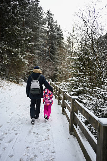 Father and daughter walking away on a snowy forest path during winter