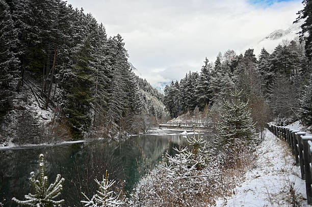 Snow-covered forest and mountains creating reflections in a serene alpine lake during winter
